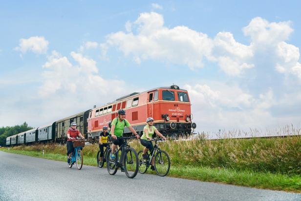Eine Gruppe Radfahrer fährt auf einer Straße neben einem „Reblaus Express“-Zug.