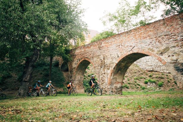 Eine Gruppe von Radfahrern fährt unter einem alten Steinviadukt hindurch.
