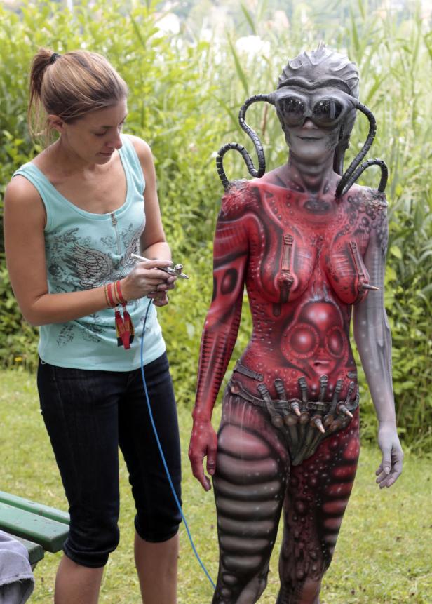 Eine Frau bemalt eine andere Frau mit einem aufwändigen Bodypainting im Stil von H.R. Giger.