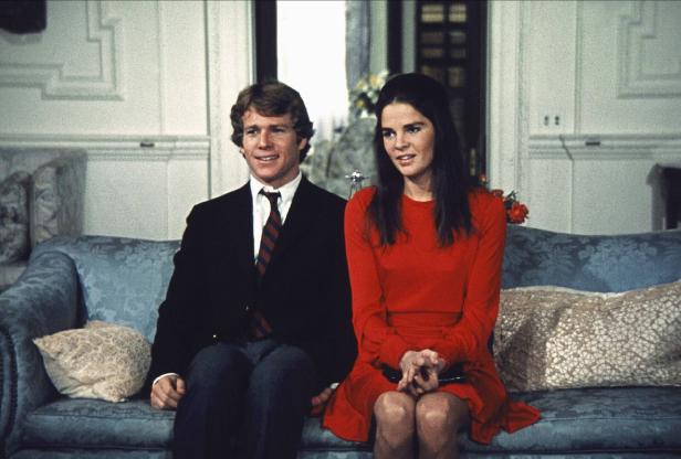 Ein Mann im Anzug und eine Frau in einem roten Kleid sitzen auf einem Sofa.