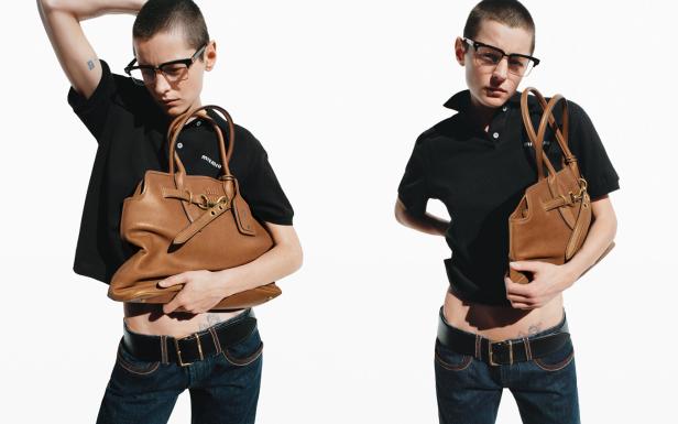 Eine Person mit Brille posiert mit einer braunen Miu Miu Handtasche vor einem weißen Hintergrund.