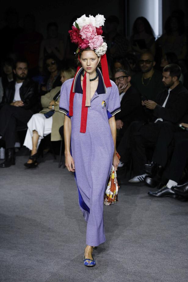 Ein Model mit einem Blumenkopfschmuck und einem hellvioletten Kleid auf einem Laufsteg.