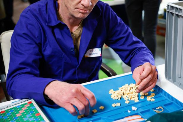 Ein Mann namens Laurent sortiert kleine Buchstabenplättchen auf einer blauen Unterlage.