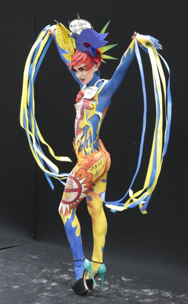 Eine Frau mit Körperbemalung zum Thema Frieden und Krieg, mit blau-gelben Bändern.