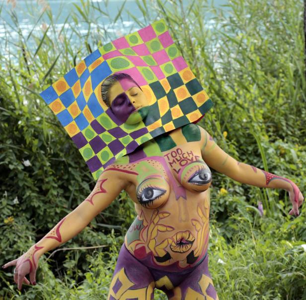 Eine Frau mit Körperbemalung posiert vor einem grünen Hintergrund.