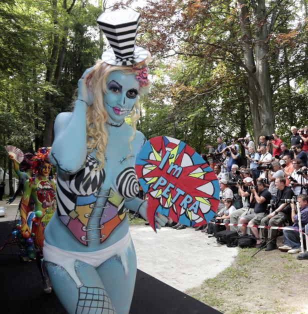 Eine blau bemalte Frau mit Zylinder hält ein Schild mit der Aufschrift „I'm Petra“ vor einer Menschenmenge.