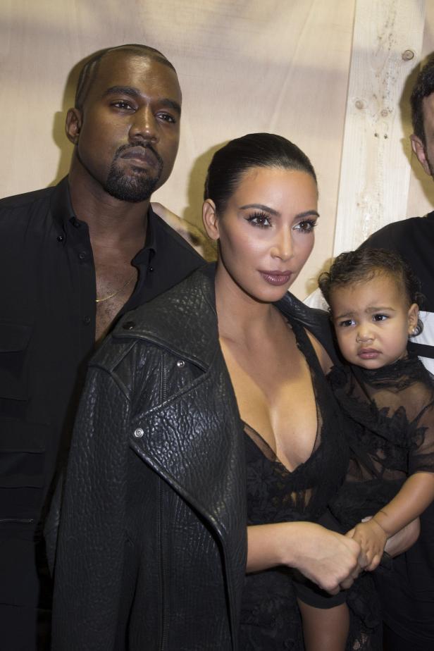 Kim Kardashian hält ihre Tochter North West, während Kanye West daneben steht.