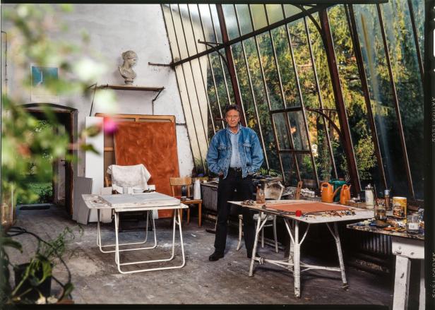 Ein Mann steht in einem Atelier mit Tischen, Leinwänden und einer großen Fensterfront.