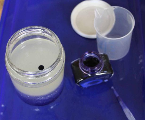 Ein Glas mit einer Flüssigkeit und Tinte auf einem blauen Untergrund.