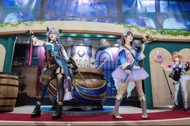 Zwei Frauen in Kostümen posieren vor einem großen Kessel für ein „Atelier“-Cosplay.