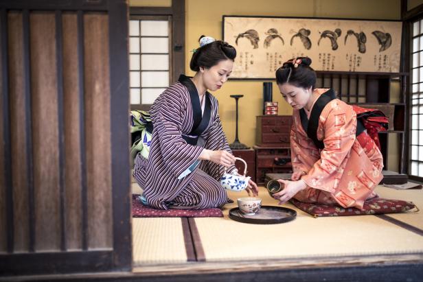 Zwei Frauen im Kimono knien auf Tatami-Matten und führen eine Teezeremonie durch.