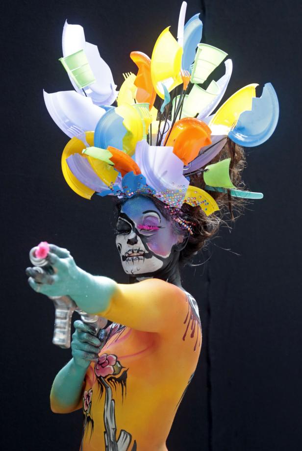 Eine Frau mit Körperbemalung und einem Kopfschmuck aus Plastikgeschirr zielt mit einer Spielzeugpistole.
