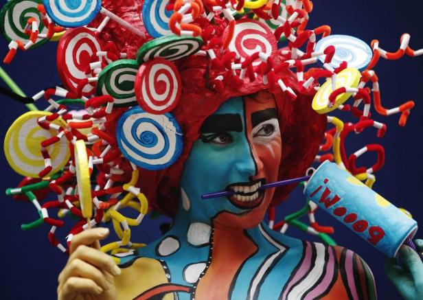 Eine Person mit Körperbemalung und einem Kopfschmuck aus Süßigkeiten posiert vor einem blauen Hintergrund.