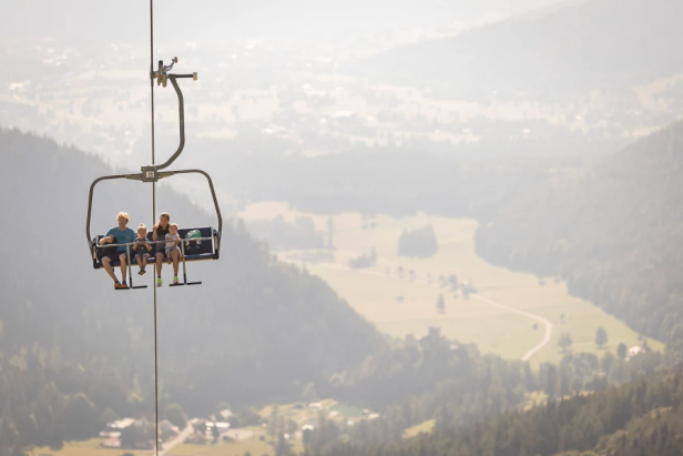Eine Familie fährt mit einem Sessellift über eine bewaldete Landschaft.