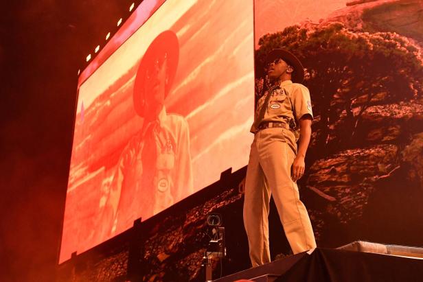 Tyler, the Creator, tritt in Khaki-Kleidung auf einer Bühne vor einer großen Leinwand auf.