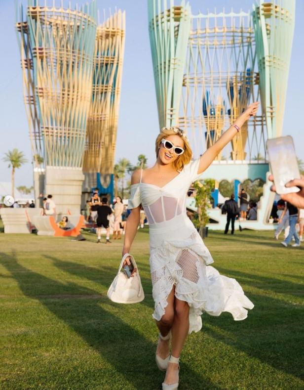 Eine Frau in einem weißen Kleid posiert vor Kunstinstallationen auf einem Festivalgelände.
