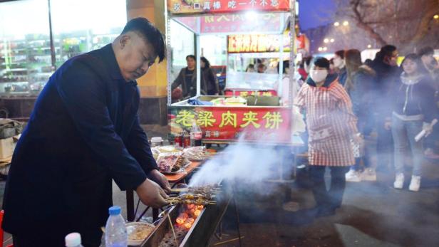Ein Mann grillt Fleischspieße an einem Straßenstand in China.