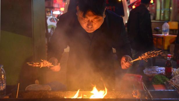 Ein Mann grillt Fleischspieße über einem offenen Feuer auf einem Marktstand.