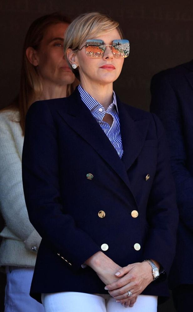 Fürstin Charlène von Monaco mit Blazer und Sonnenbrille, in der sich ein Tennisplatz spiegelt.