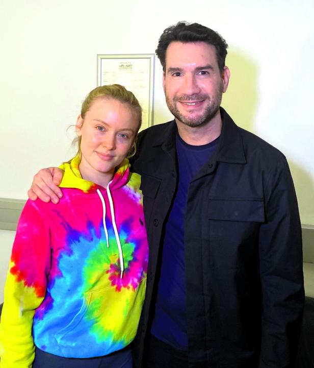 Eine junge Frau mit einem bunten Hoodie posiert mit einem Mann in einer dunklen Jacke.