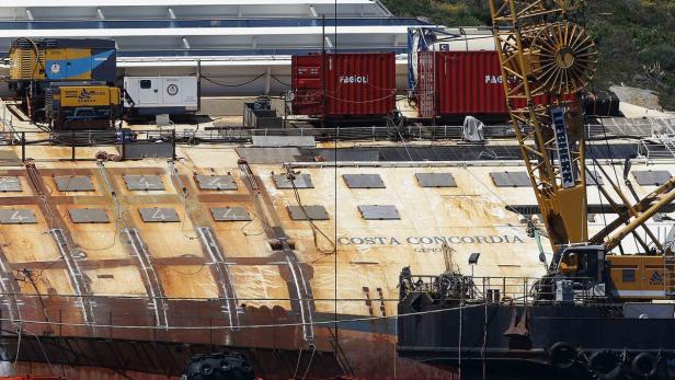 Die teilweise abgetragene „Costa Concordia“ mit Baugeräten und Containern an Deck.