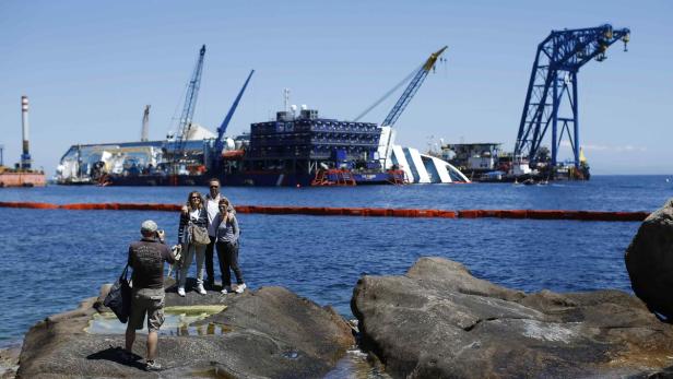 Eine Gruppe von Menschen posiert vor dem teilweise versunkenen Schiff Costa Concordia.
