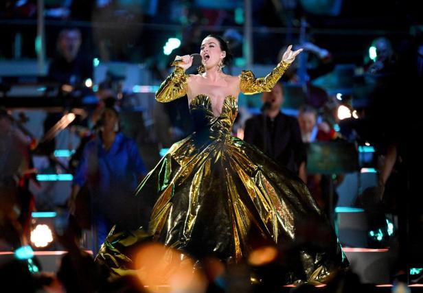 Katy Perry tritt in einem goldenen Kleid auf einer Bühne auf.