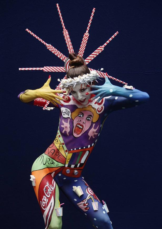 Eine Frau mit Körperbemalung posiert vor einem blauen Hintergrund.