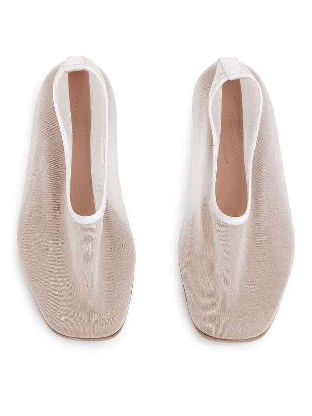 Ein Paar beigefarbene Stoffschuhe mit weißen Akzenten auf weißem Hintergrund.