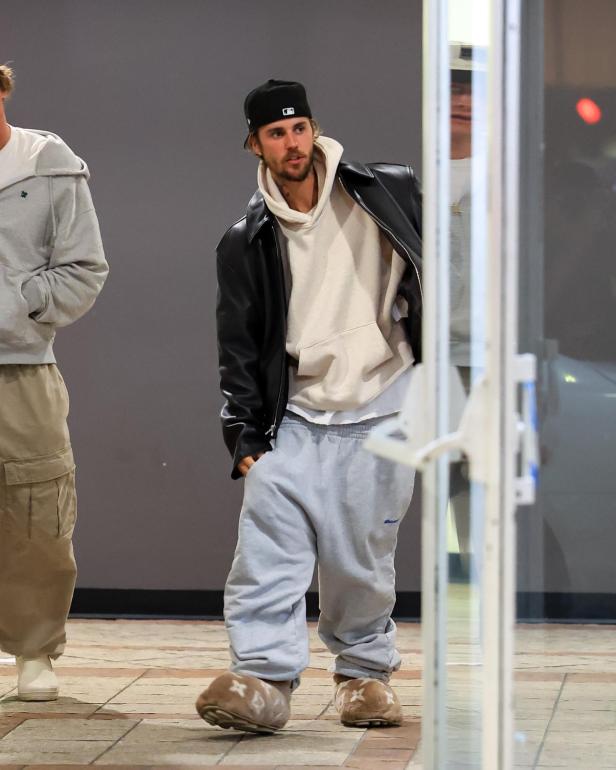 Justin Bieber trägt eine schwarze Jacke, einen Hoodie und Hausschuhe.