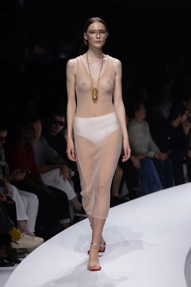 Ein Model mit futuristischer Brille und transparentem Kleid auf einem Laufsteg.