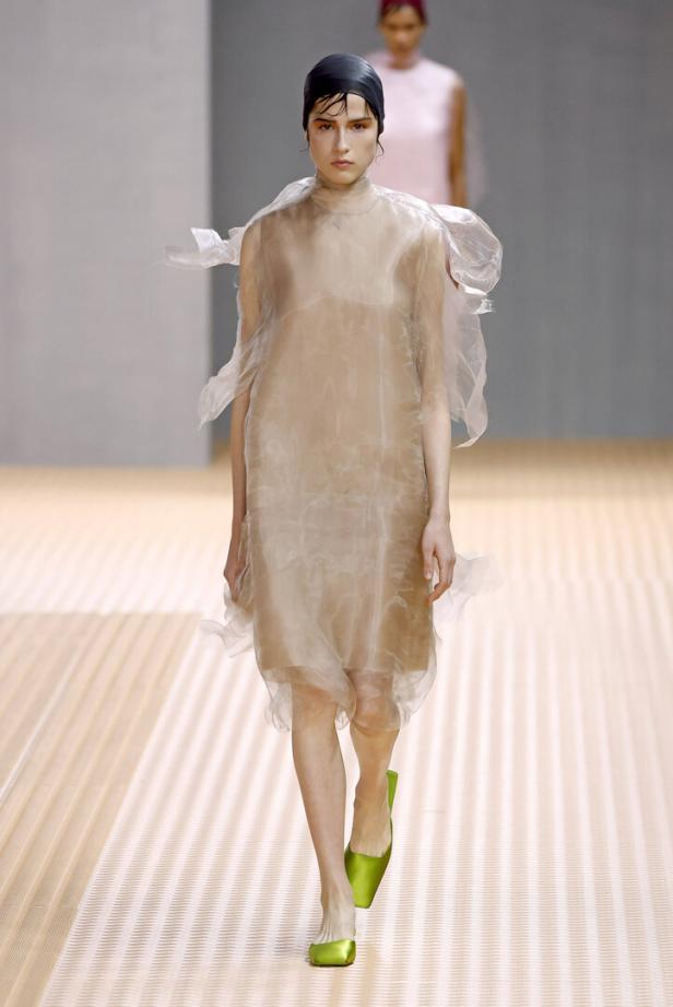 Ein Model auf dem Laufsteg, gekleidet in ein transparentes Kleid und grüne Schuhe.