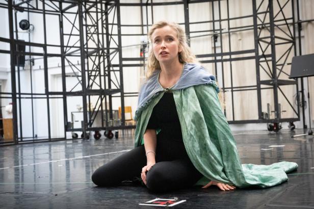 Eine Schauspielerin in einem grünen Umhang sitzt auf der Bühne, möglicherweise während einer Aufführung von „Phantom der Oper“.