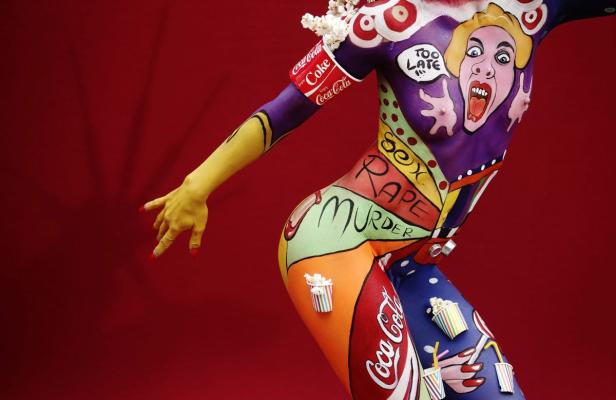 Ein Körper ist mit provokanten Bildern und Slogans bemalt, darunter Coca-Cola-Logos und die Worte „Sex“, „Rape“ und „Murder“.