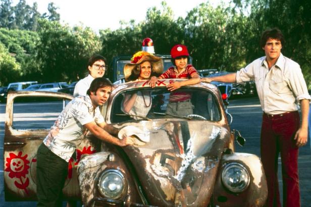 Die Besetzung des Films „Herbie Goes Bananas“ posiert mit einem verrosteten VW Käfer.