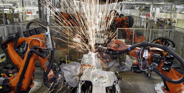 Orangefarbene Roboter schweißen in einer Fabrik eine Karosserie zusammen, wobei Funken fliegen.