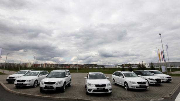 Mehrere weiße Škoda-Fahrzeuge stehen auf einem Parkplatz unter bewölktem Himmel.
