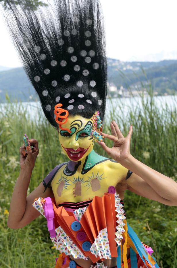 Eine Person mit aufwendiger Körperbemalung und extravagantem Haar posiert im Freien.