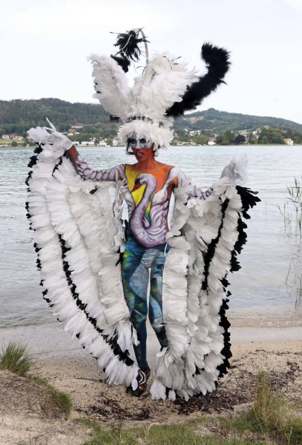 Eine Frau mit Körperbemalung und Federn steht am Ufer eines Sees.