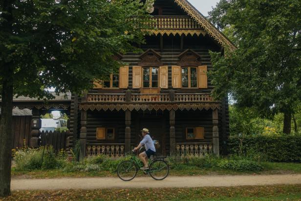 Ein Mann fährt mit dem Fahrrad vor einem traditionellen russischen Holzhaus.