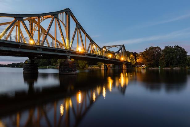 Die Glienicker Brücke in Potsdam bei Dämmerung mit Spiegelungen im Wasser.