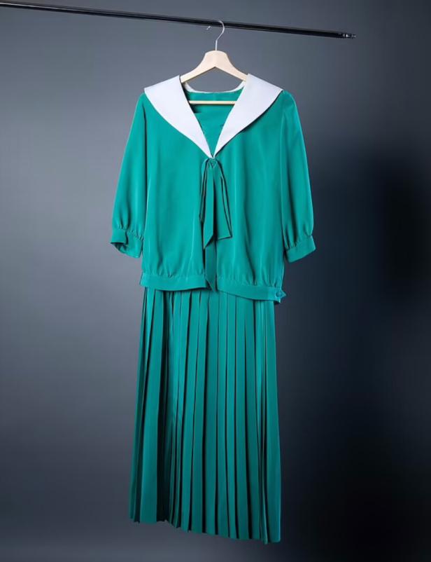 Ein grünes Kleid mit weißem Kragen hängt an einem Kleiderbügel.