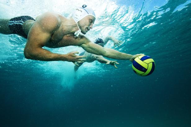 Zwei Männer spielen Wasserball im Meer, mit Kappen, tauchen und jagen dem Ball nach