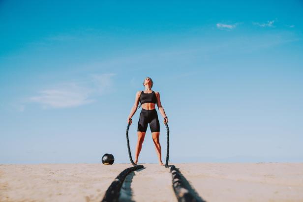 Frau in Sportkleidung am Strand und trainiert mit Seil und Medizinball
