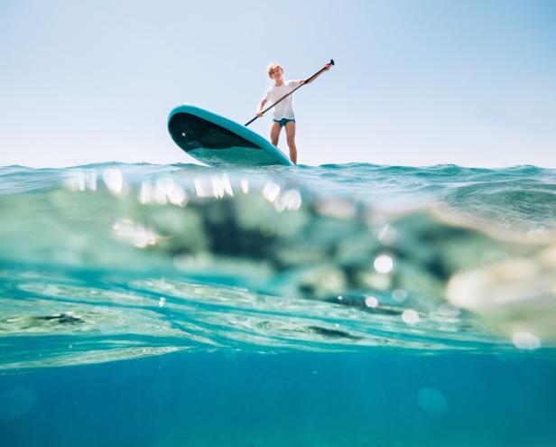 Unterwasser Perspektive auf einen blonden Teenager auf einem Stand Up Paddel im Meer