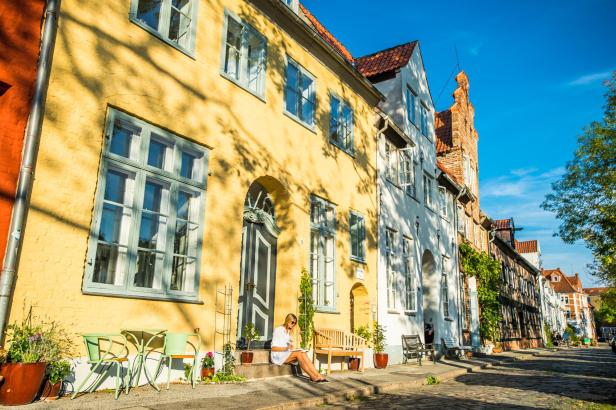 Eine Frau sitzt vor einem gelben Haus in der Sonne und liest ein Buch.