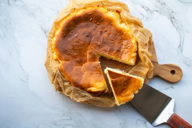 Ein baskischer Käsekuchen mit einem Stück, das herausgeschnitten wurde, liegt auf einem Schneidebrett.
