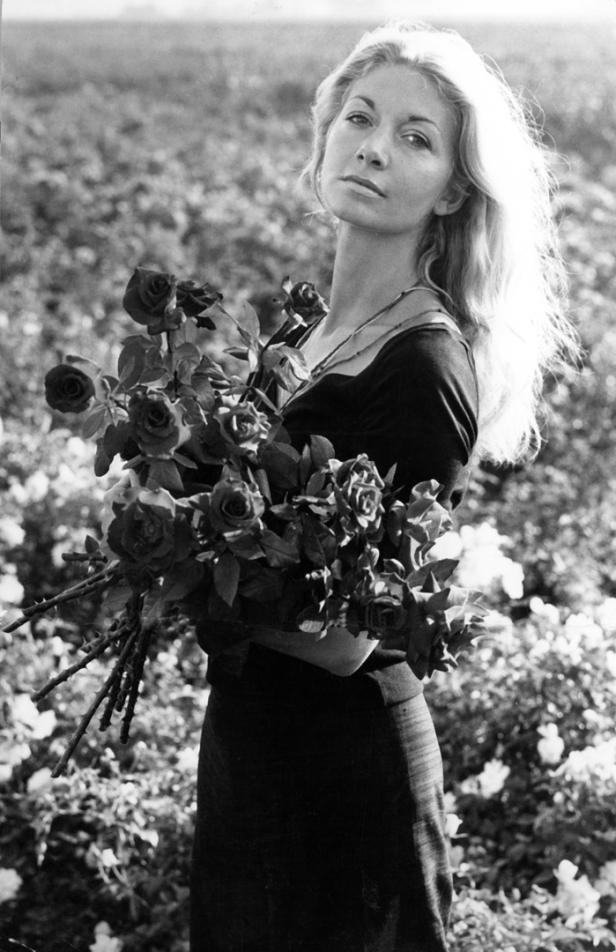 Eine Frau mit blonden Haaren hält einen Strauß Rosen in einem Feld.