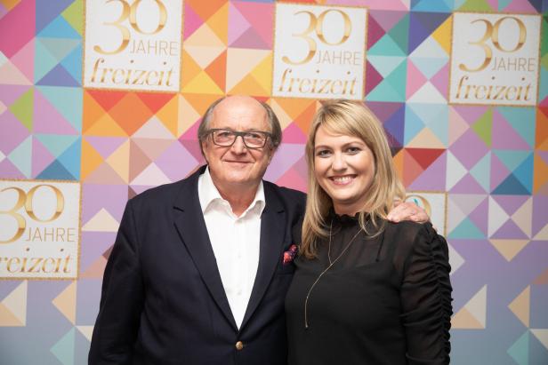 Ein Mann und eine Frau posieren vor einem Hintergrund mit der Aufschrift „30 Jahre Freizeit“.