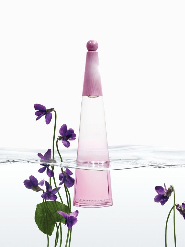 Ein Flakon „Eau d'Issey Solar Violet“ steht im Wasser, umgeben von Veilchen.